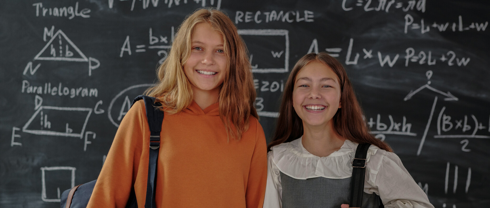 Two girls standing together in a classroom, smiling at the camera'